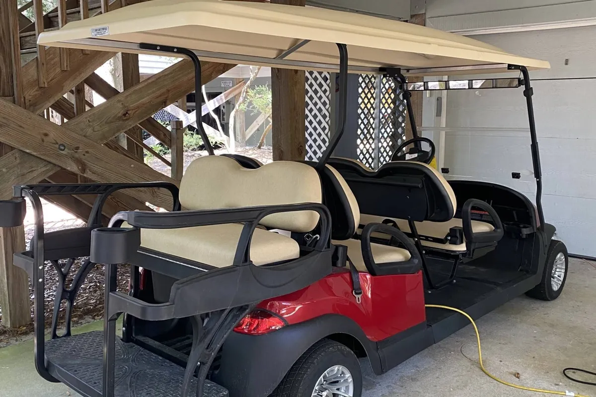 A golf cart is parked near wooden stairs in a garage-like setting, representing a popular mode of transportation on Bald Head Island. The scene hints at adventure and easy access to club amenities, evoking a playful and inviting mood.
