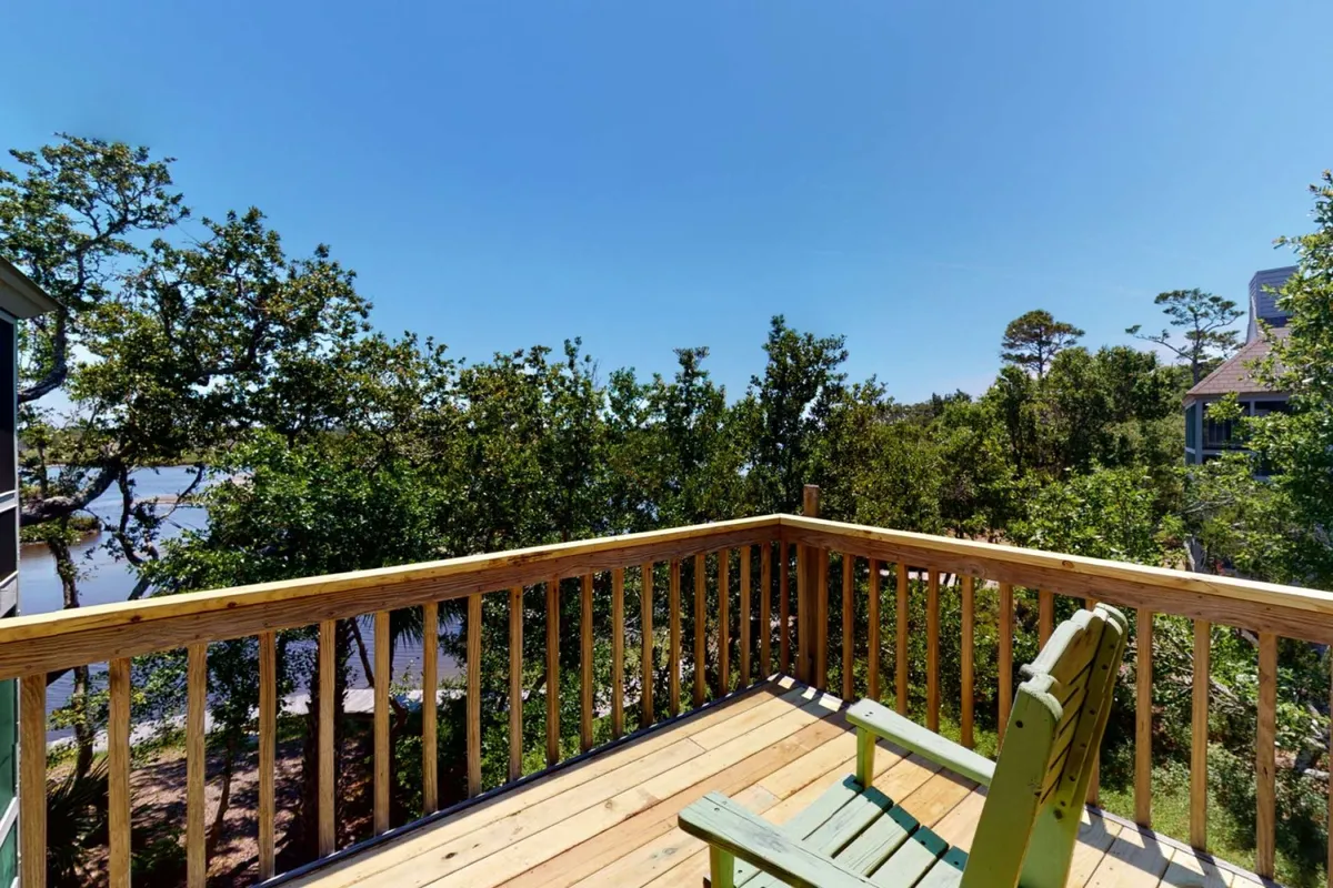 The photo captures a serene wooden deck with a green chair, lush greenery, and a peaceful marsh view—a classic screened-in or outdoor porch setting that blurs the line between inside and nature.