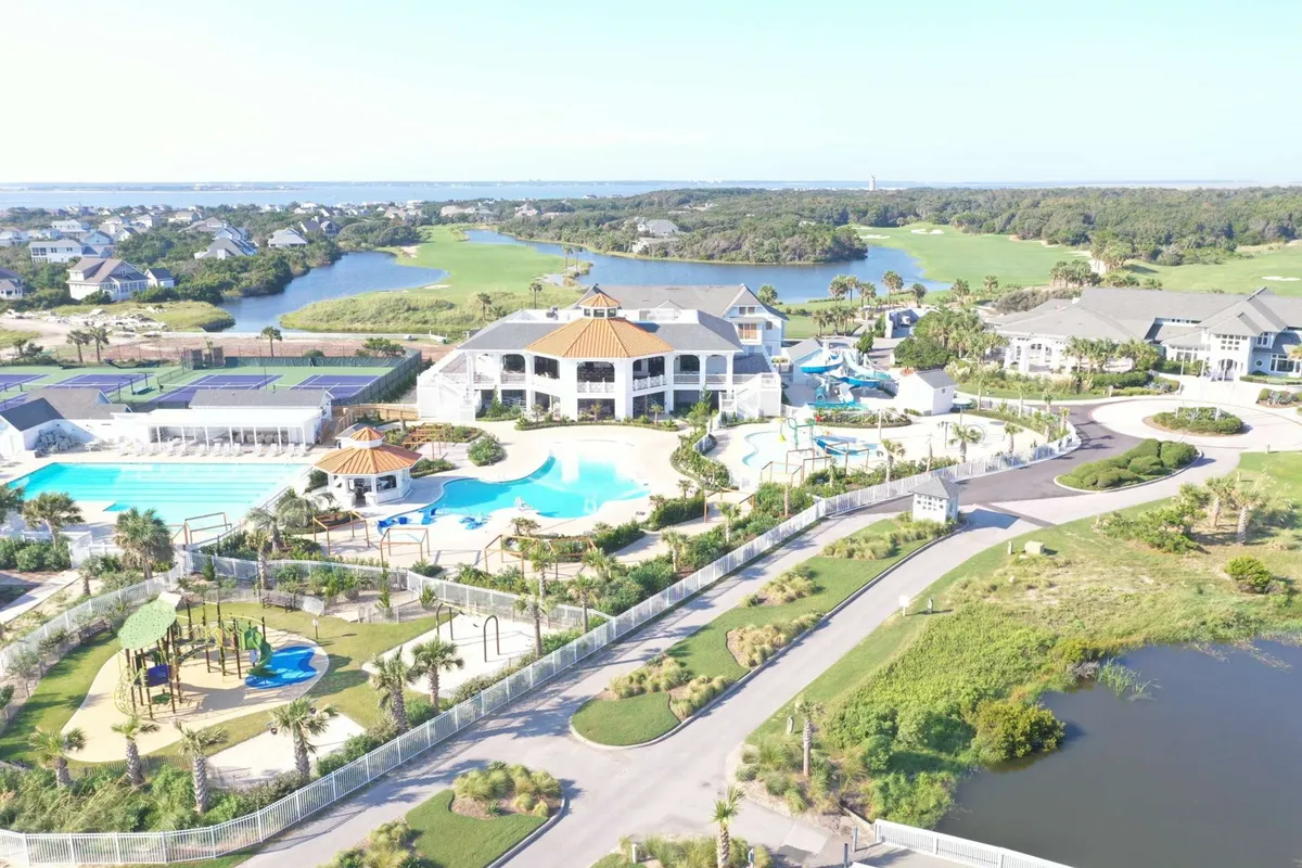 A spacious outdoor pool area featuring a large saltwater pool, water slides for children, a clubhouse in the background, and a playground set amid lush landscaping. Families are enjoying the water, and the lively scene is set during daylight, evoking a joyful and carefree mood.