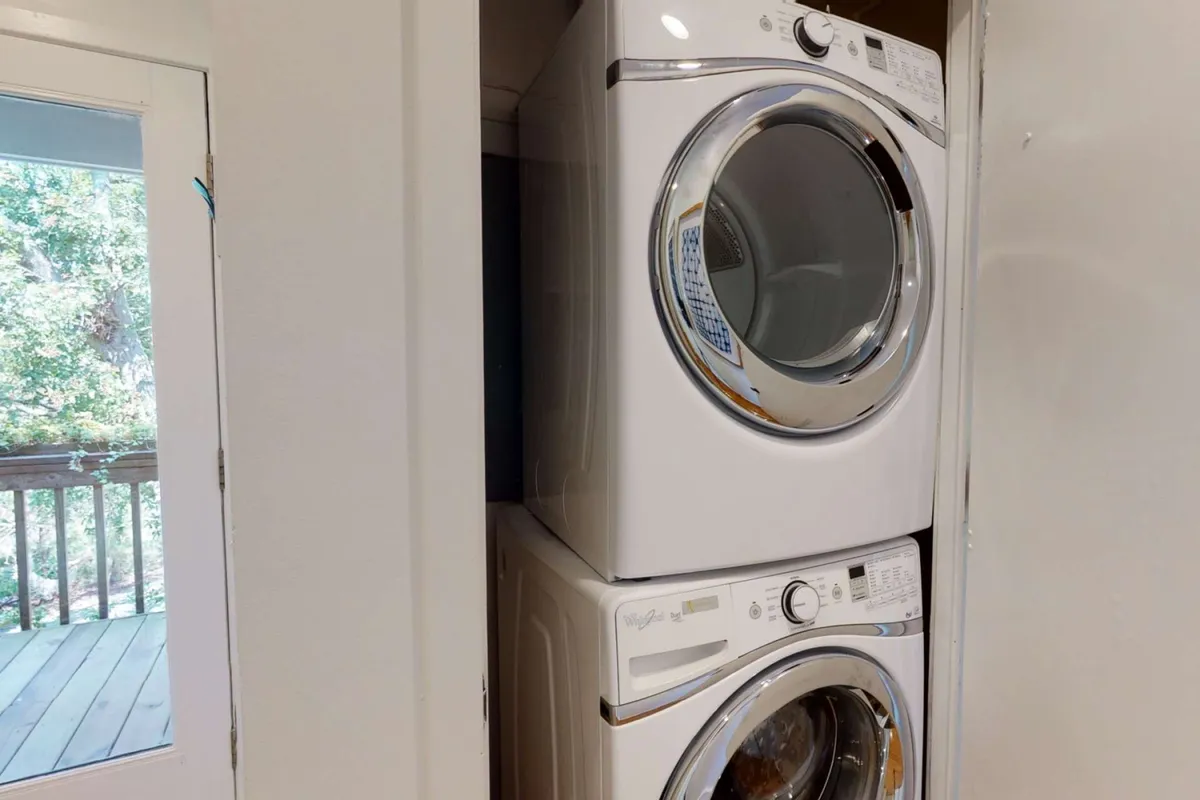 A bright, practical laundry area featuring a stacked washer and dryer is complemented by a window bringing in natural light. The tidy setup signals convenience and makes it easy to manage outdoor gear and beachwear.