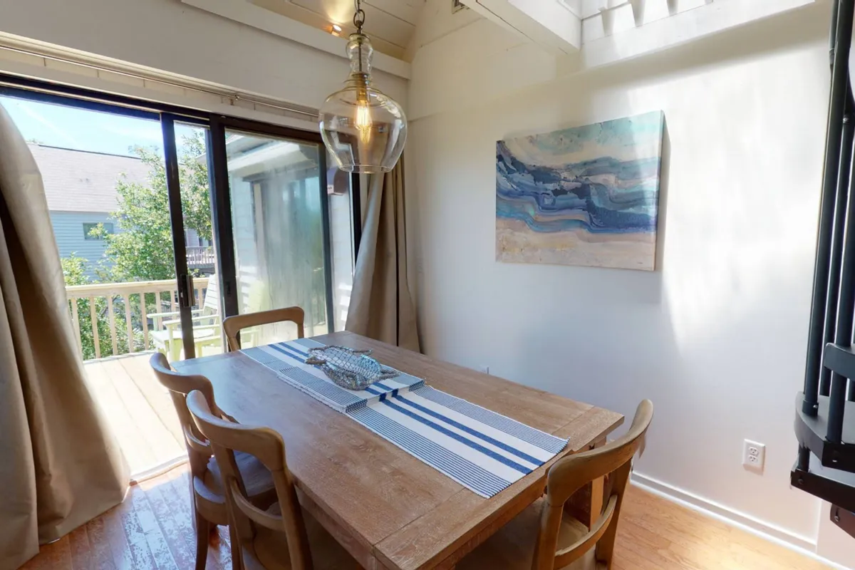 A dining area set by a large glass door, complemented by an eye-catching art piece on the wall. The space is bright and airy, with a view that hints at the outdoors—perfect for meals accompanied by nature's backdrop and the flow between dining and living spaces.