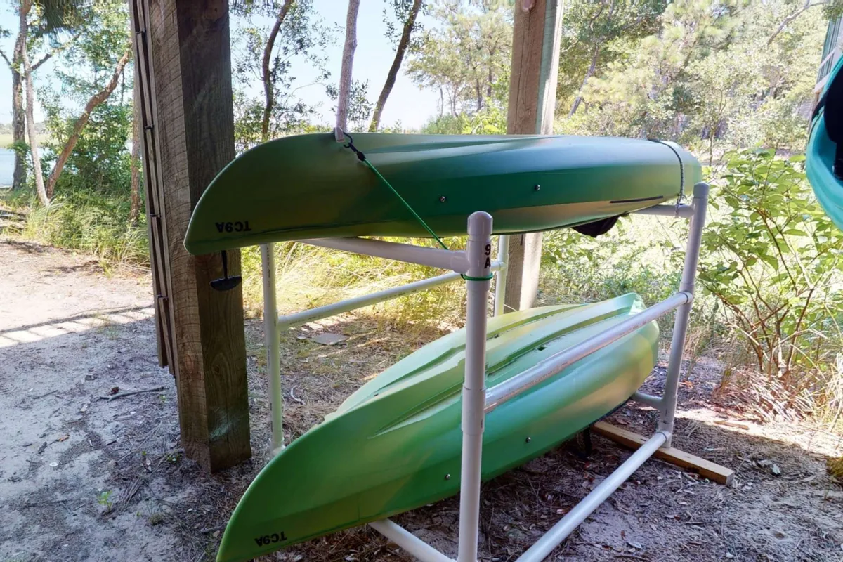 A set of bright green kayaks rests on a durable support structure amidst nature, with trees and water nearby. The setting invites guests to grab the kayaks and set out for an adventure, reflecting the ease of access and readiness for water activities.
